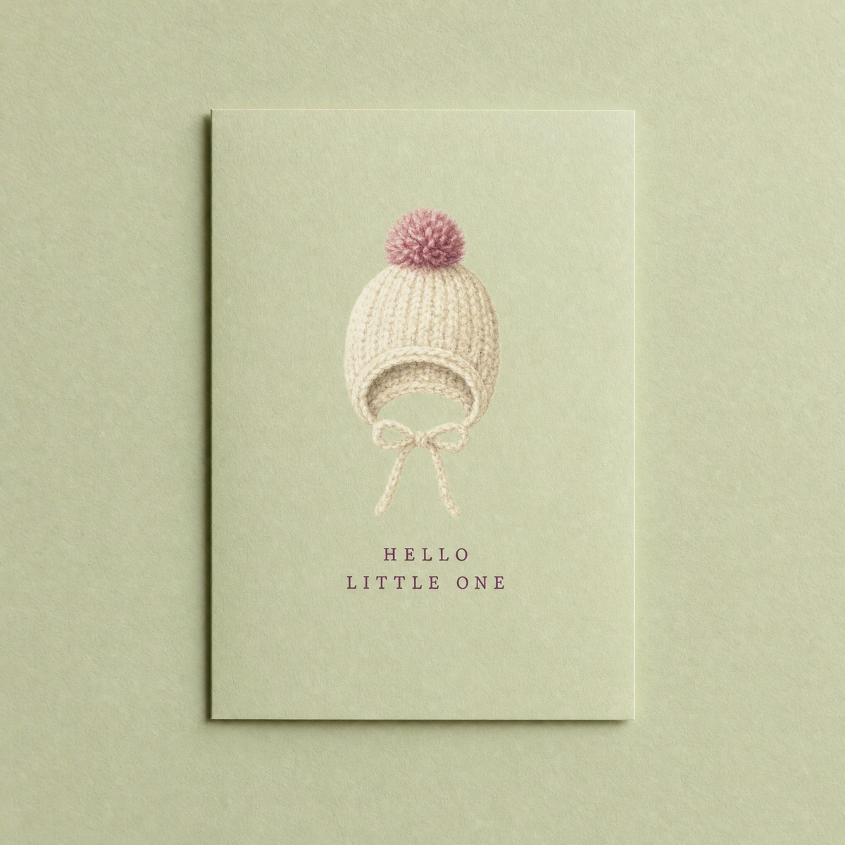 Hello Little One card: a knitted cream bonnet with a dusty rose pompom painted on a pale sage A6 card